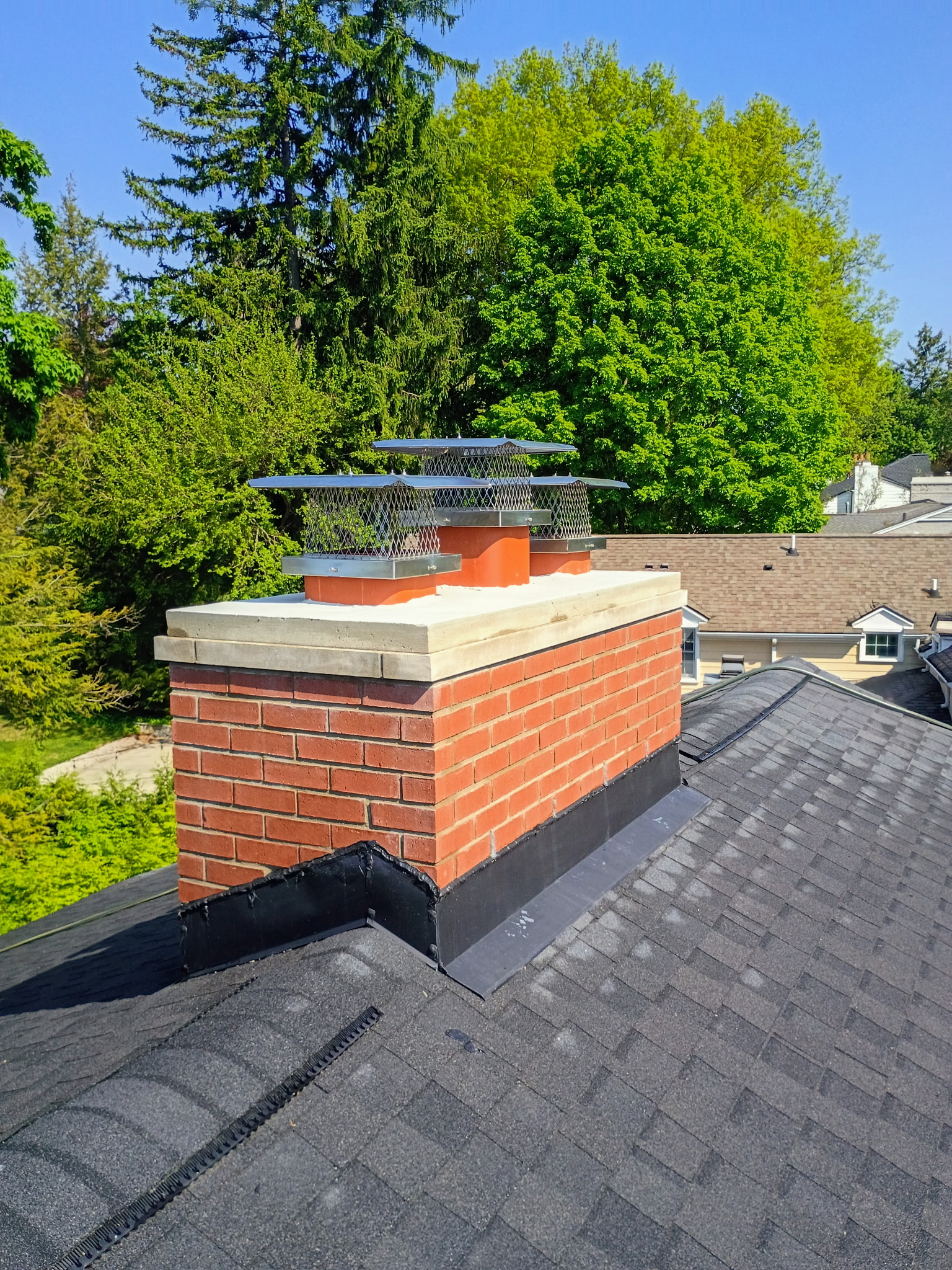 Freshly rebuilt red brick chimney with stainless caps against blue sky — Grey Oaks Chimney